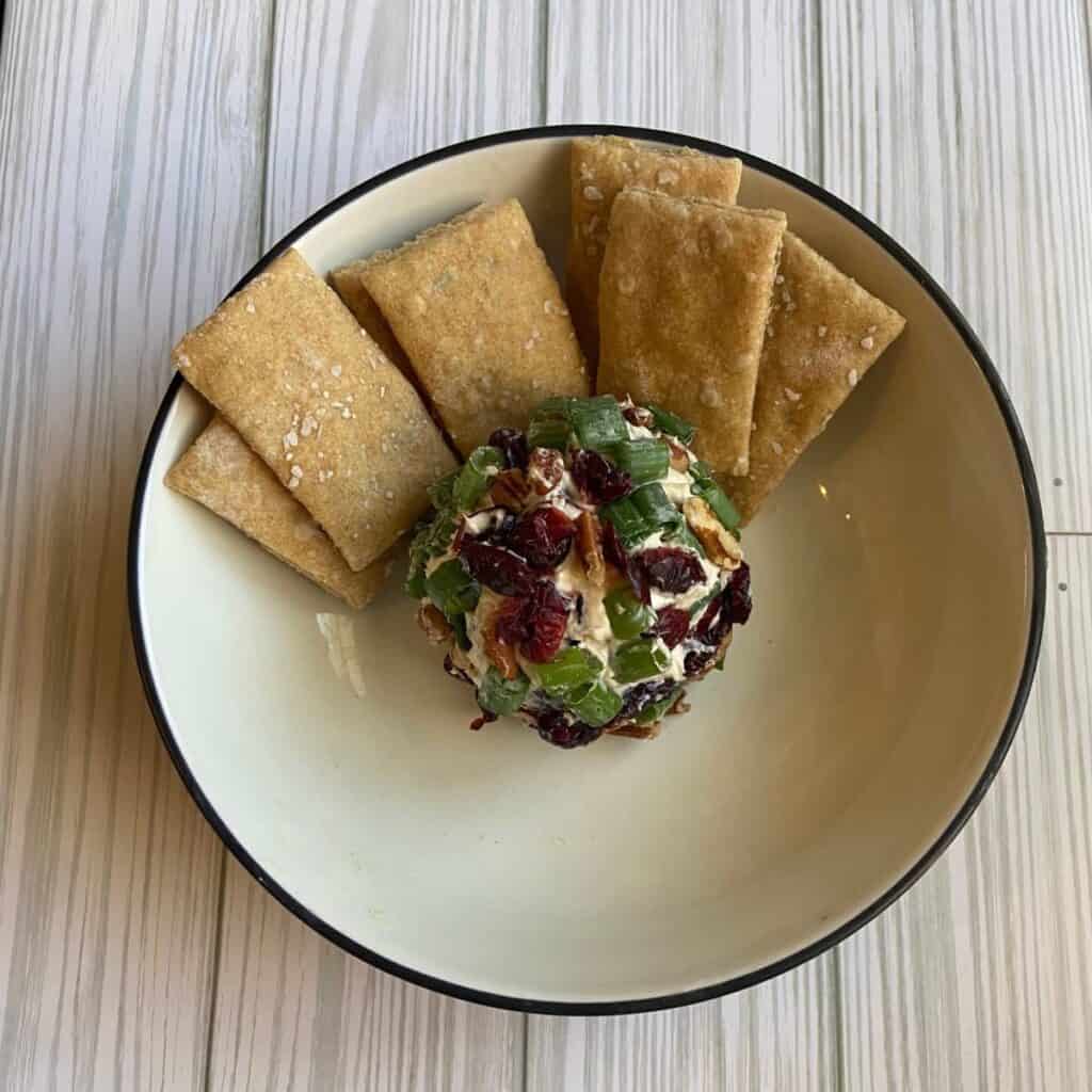 Holiday cheese ball with goat cheese, cranberries, green onion, and pecans served in a bowl with crackers.